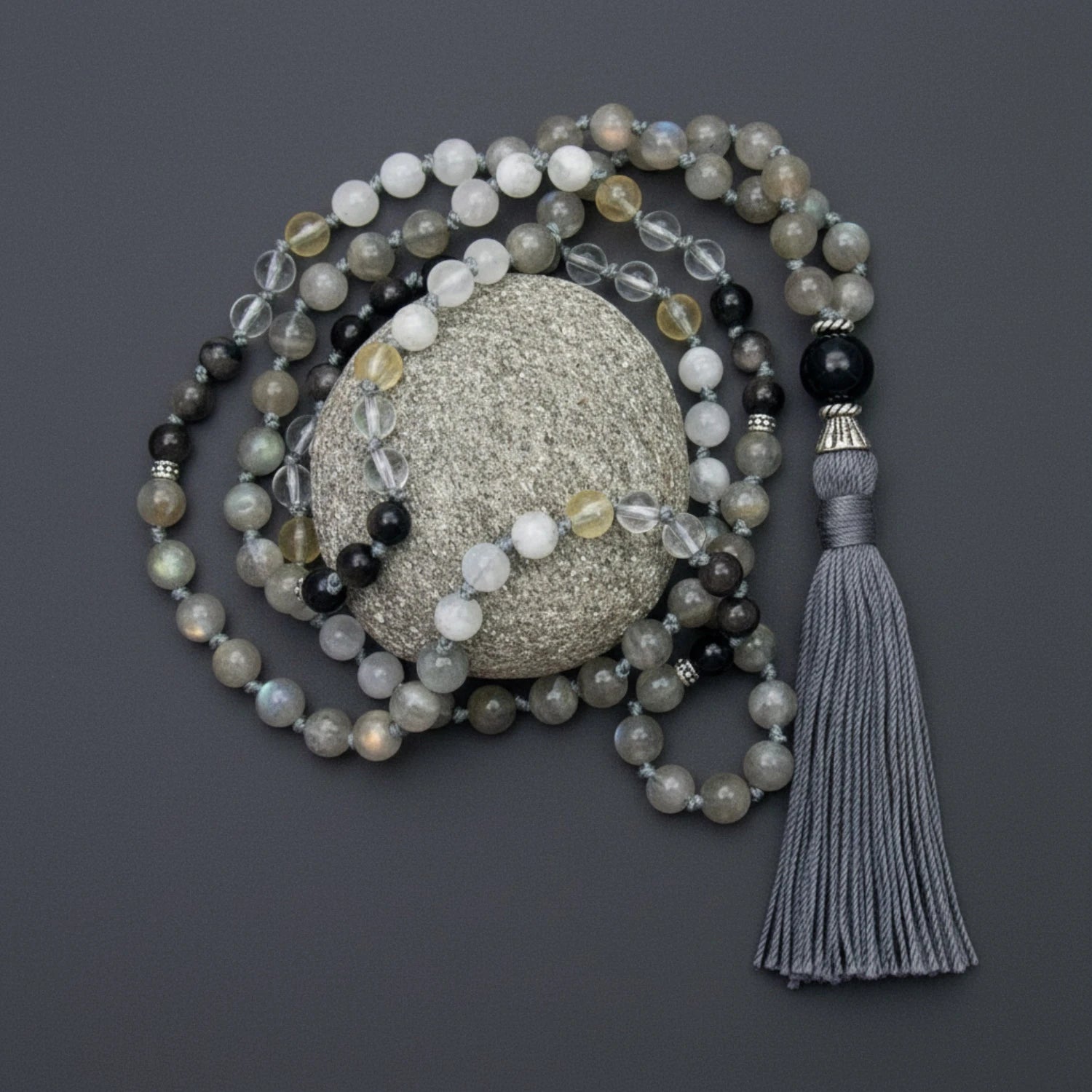 Labradorite gemstone mala necklace with moonstone, quartz, and citrine with tassel on a textured stone against a dark background
