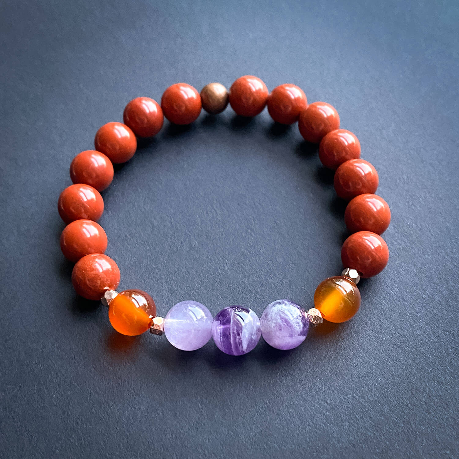 Red jasper round beaded bracelet with carnelian and amethyst on a dark background