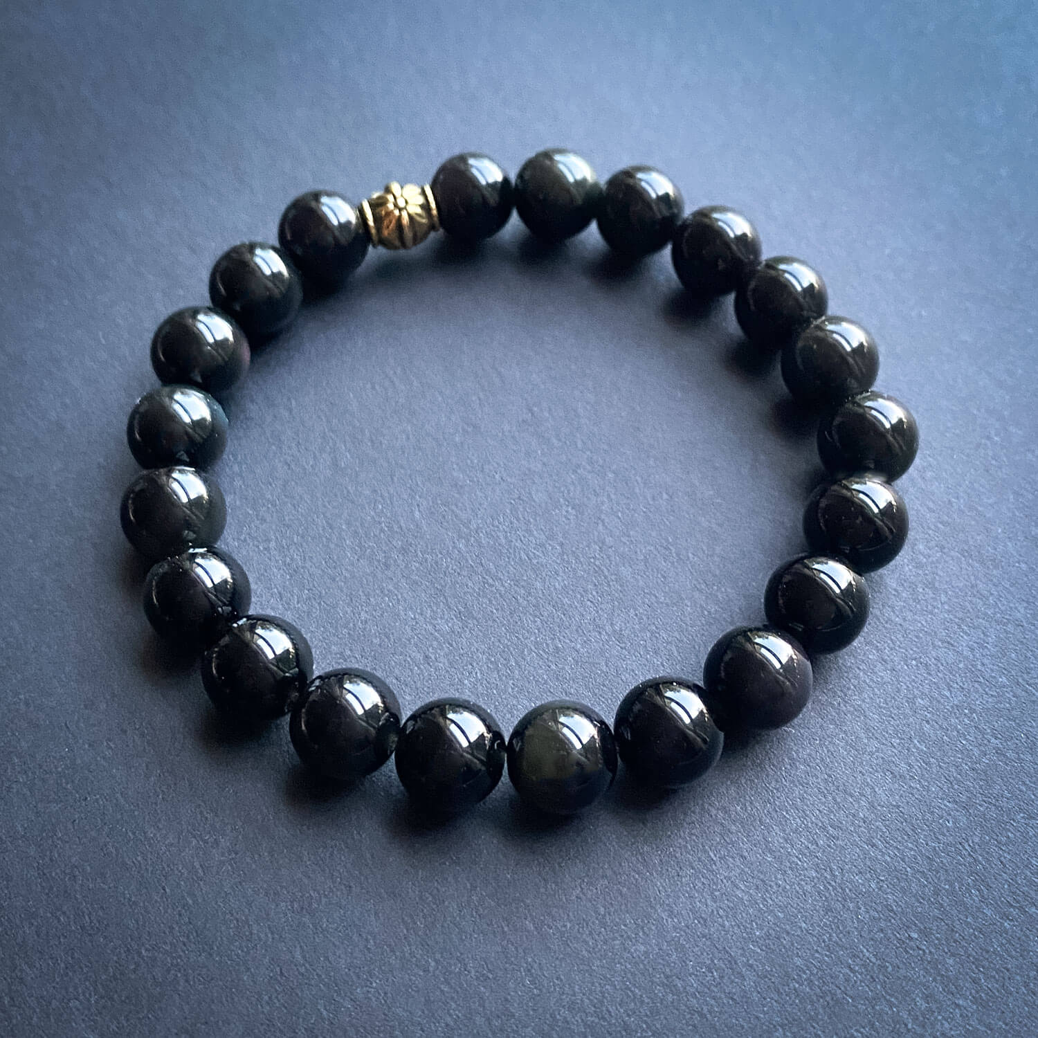 Black beaded bracelet with a gold accent bead on a dark background