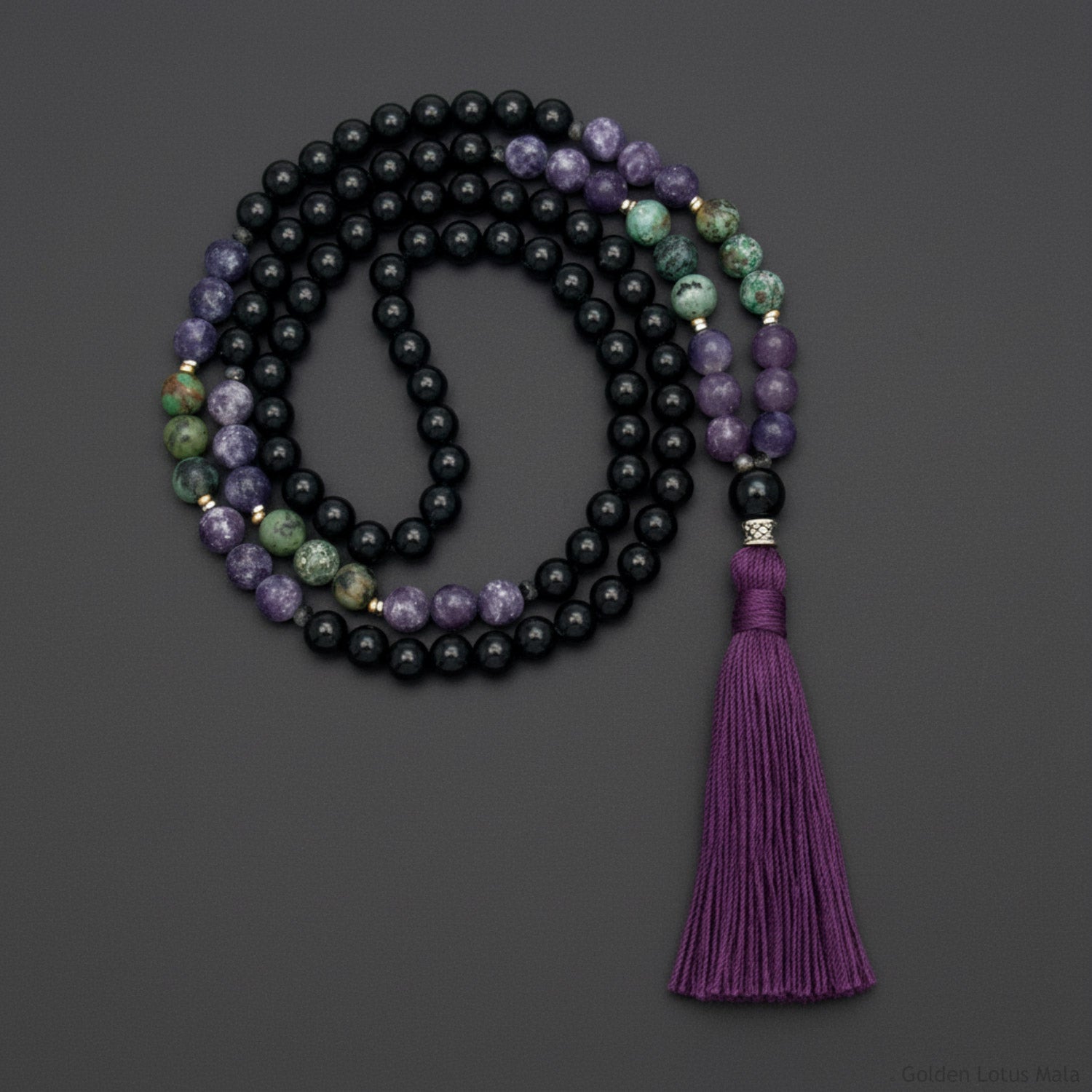 Mala necklace with black beads and a purple tassel on a dark background