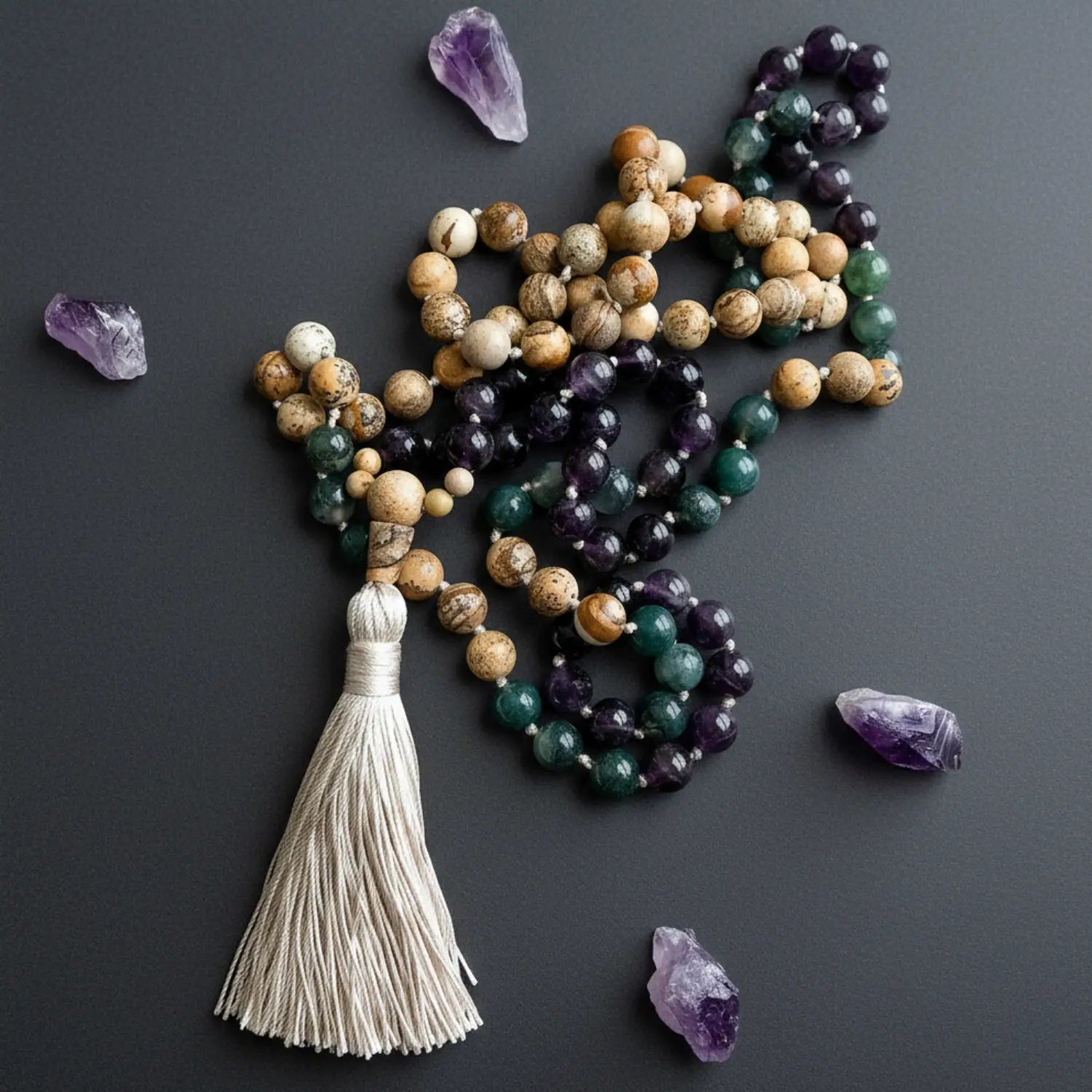 Mala necklace with beads and tassel on a dark surface with amethyst crystals