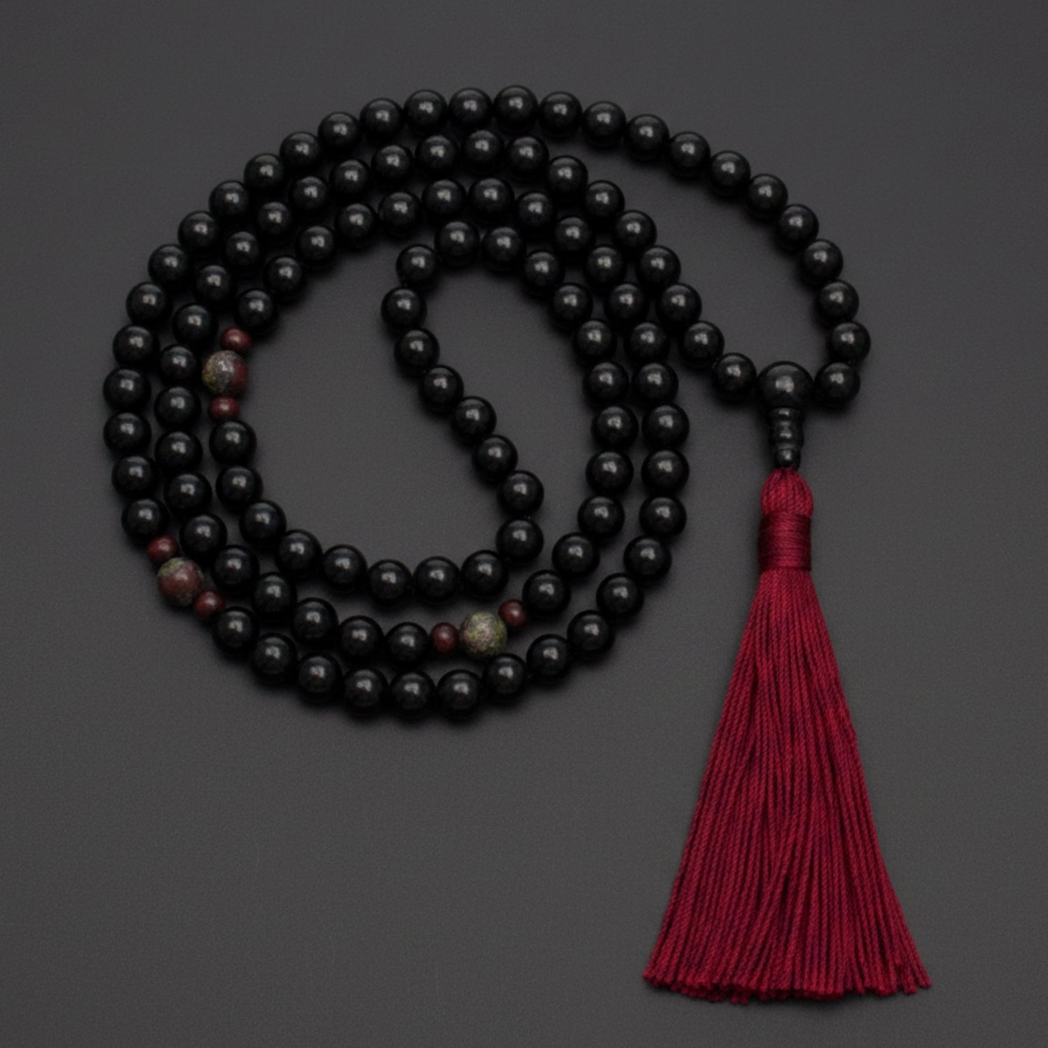 Black onyx mala necklace with a red tassel on a dark background