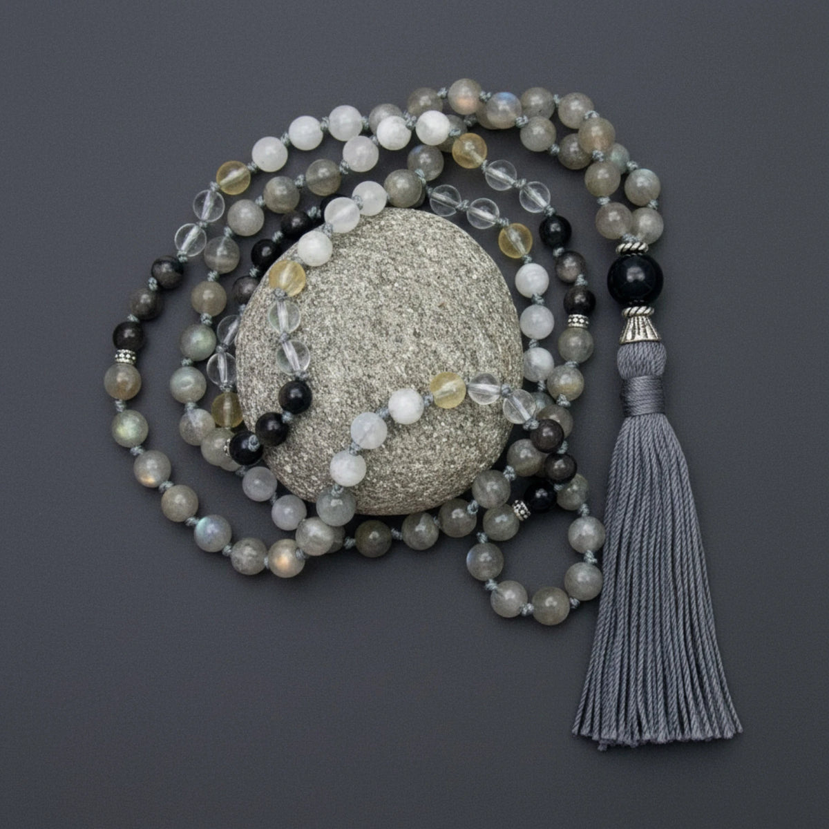 Labradorite gemstone mala necklace with moonstone, quartz, and citrine with tassel on a textured stone against a dark background