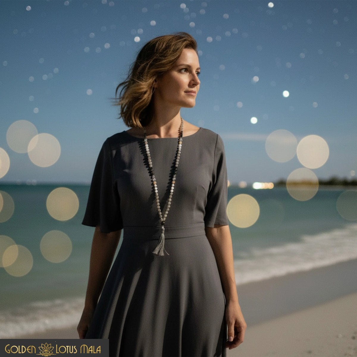 Woman standing on a beach wearing a gray dress and the Celestial Renewal Mala necklace