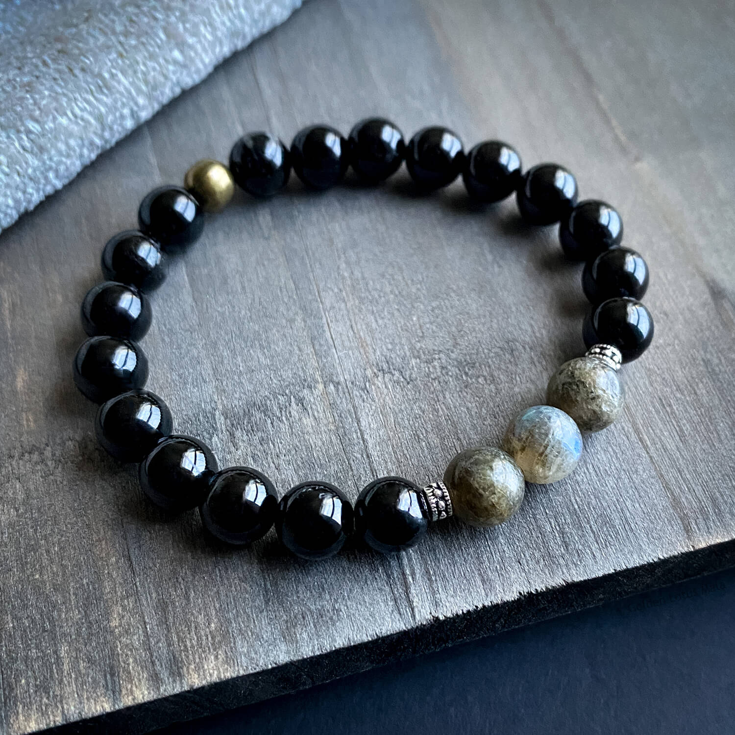 A bracelet with black tourmaline and labradorite beads on a stretch cord, displayed on a wooden surface.