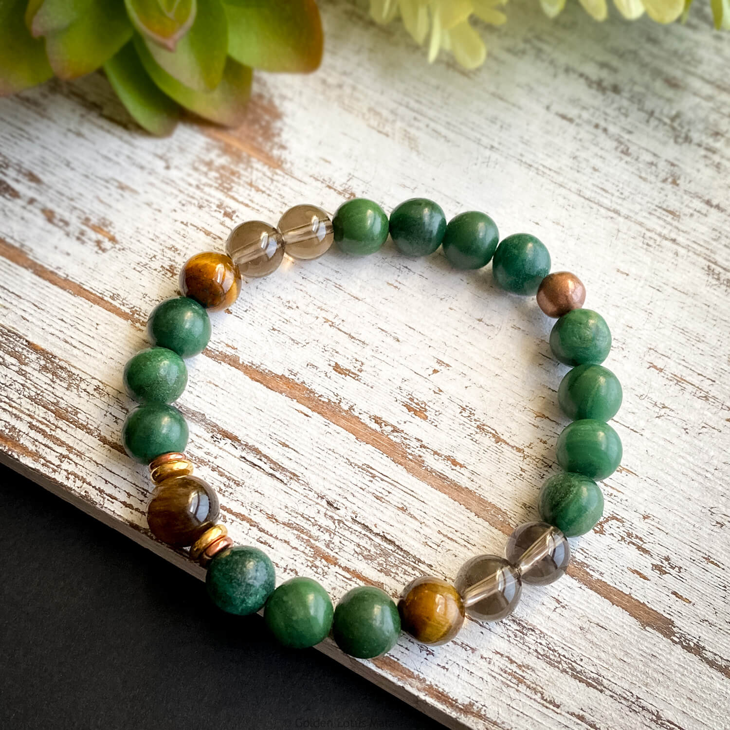 A gemstone bracelet with a mix of green, brown, gray, and gold colored beads, strung on a professional quality stretch cord.