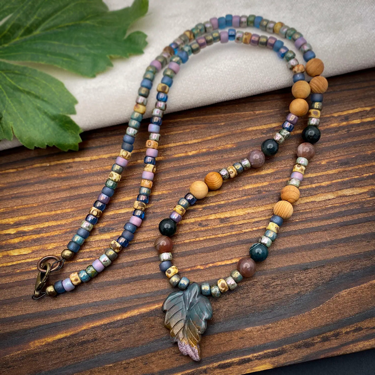 Beaded necklace with a leaf pendant on a wooden surface