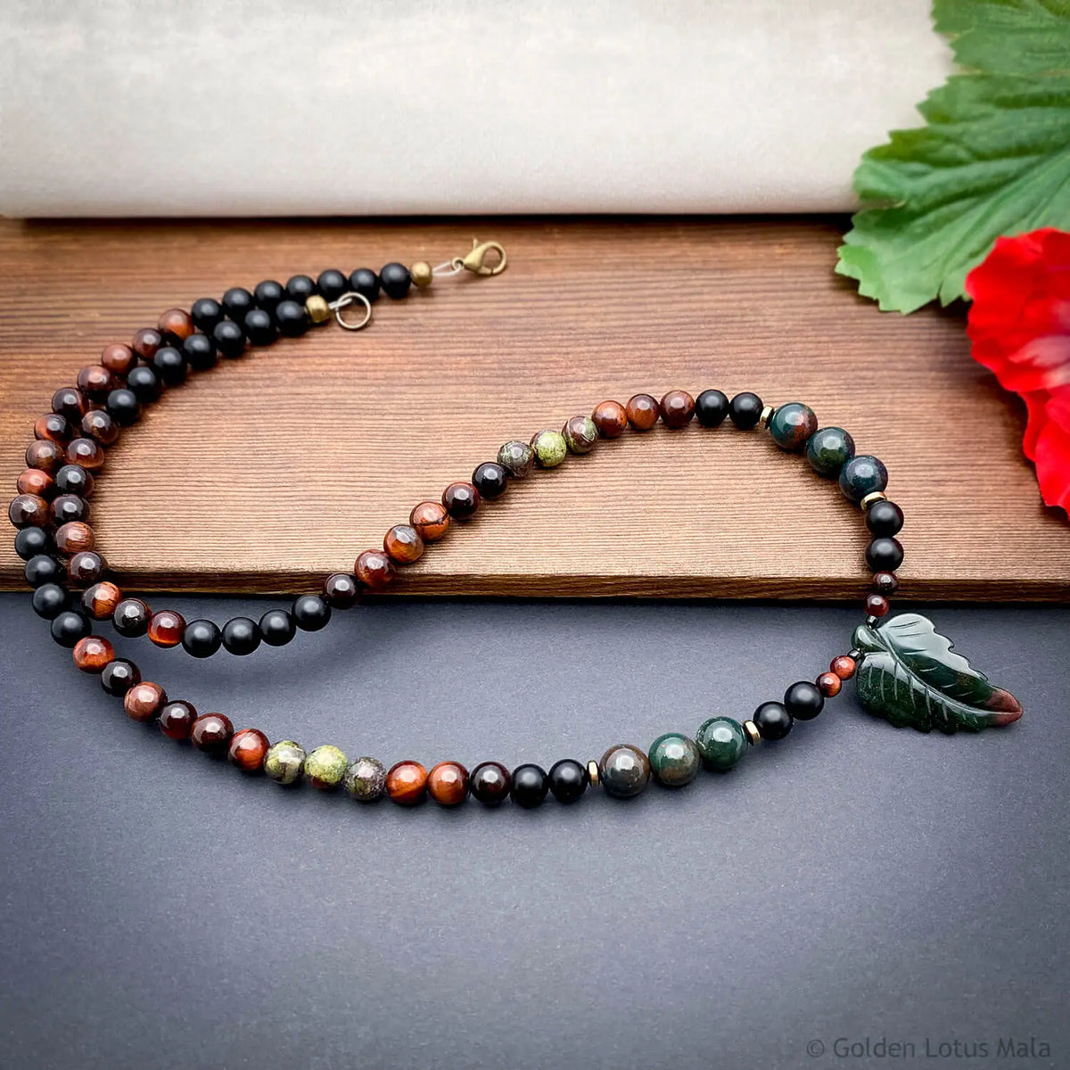 Multicolored beaded necklace on a wooden surface with a carved leaf pendant.