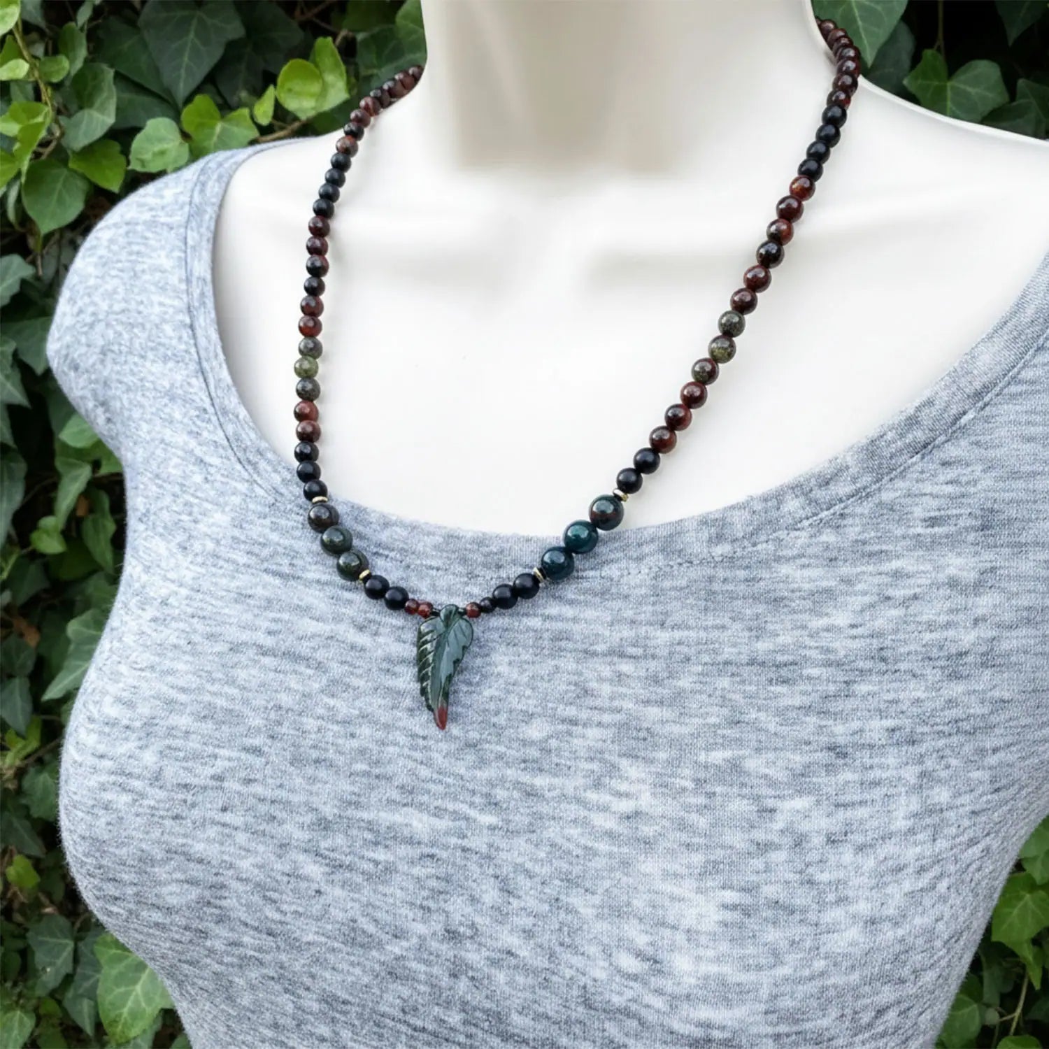 Necklace with leaf pendant on a mannequin against a green leafy background