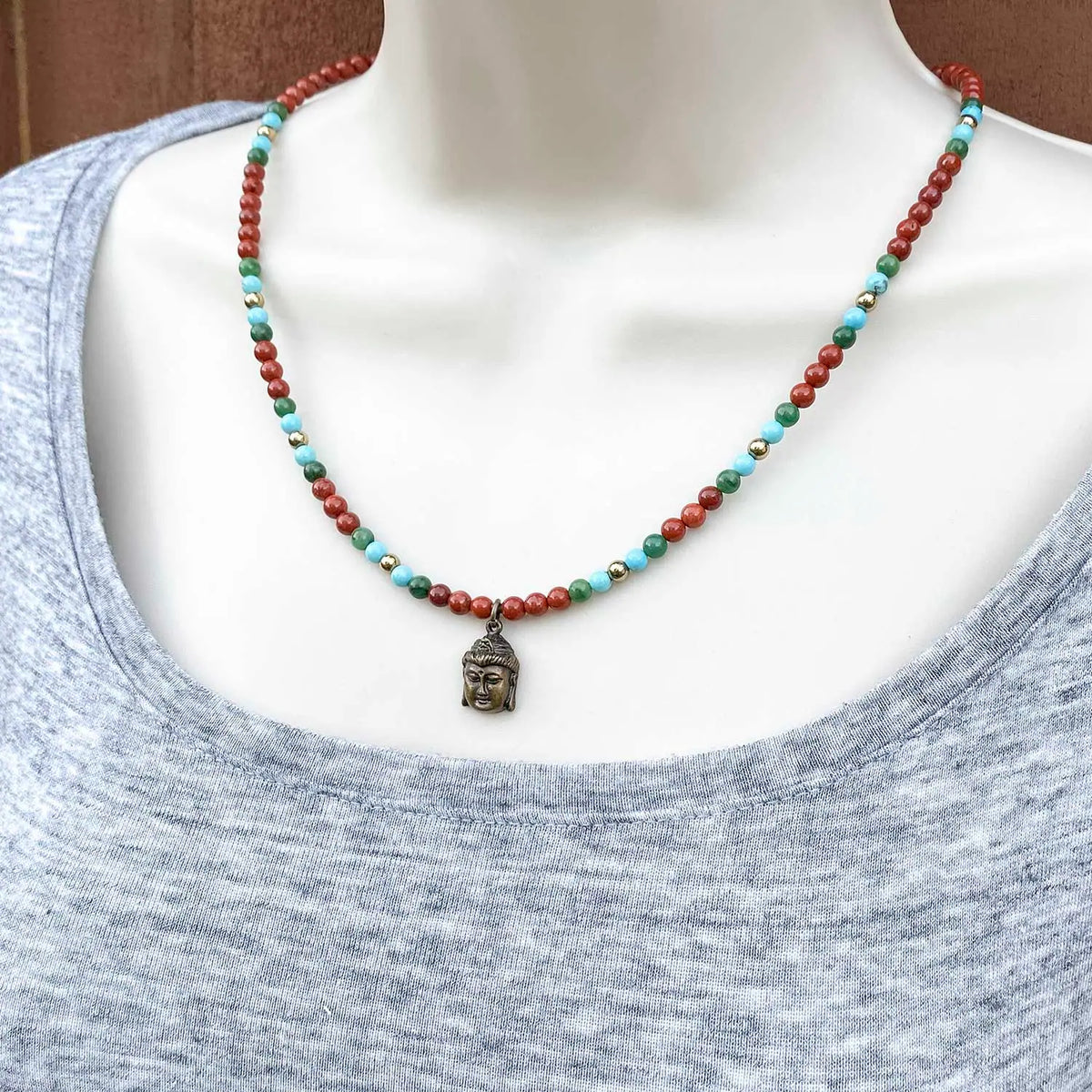 Necklace with a Buddha pendant and red, turquoise, and green dainty beads on a mannequin.