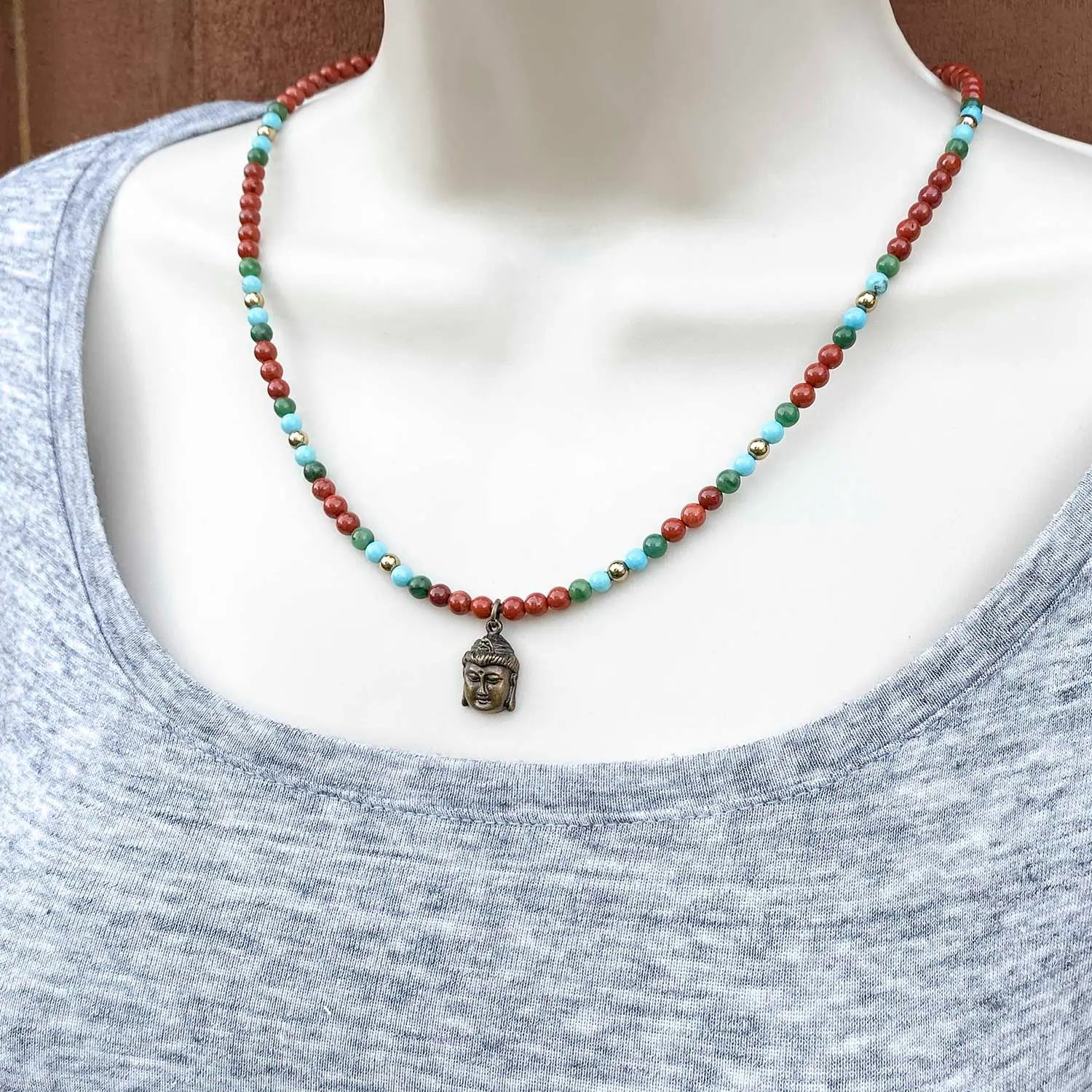 Necklace with a Buddha pendant and red, turquoise, and green dainty beads on a mannequin.