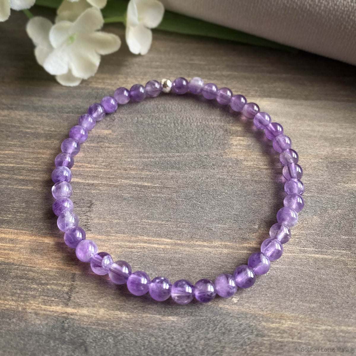 Purple amethyst beaded bracelet on a wooden surface with white flowers in the background