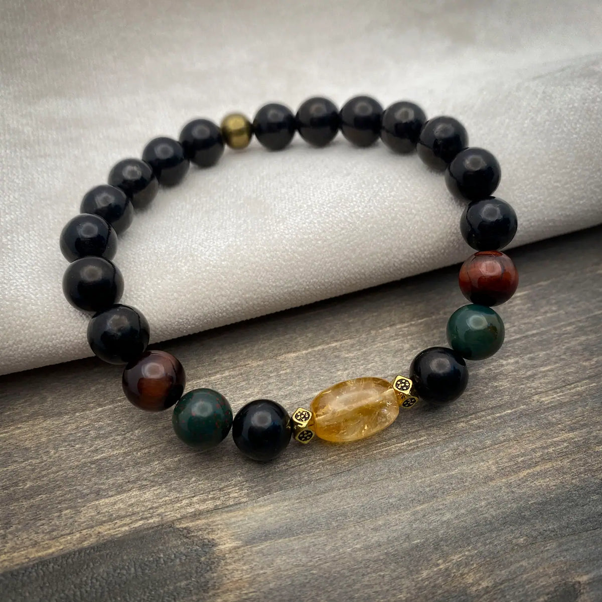 Beaded bracelet with Shungite, Bloodstone, Tigereye, and Citrine beads on a wooden surface