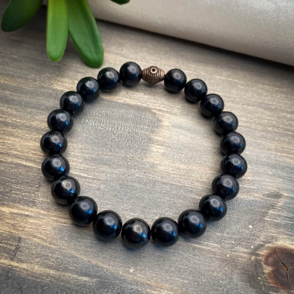 A black Shungite bracelet displayed on a wooden table