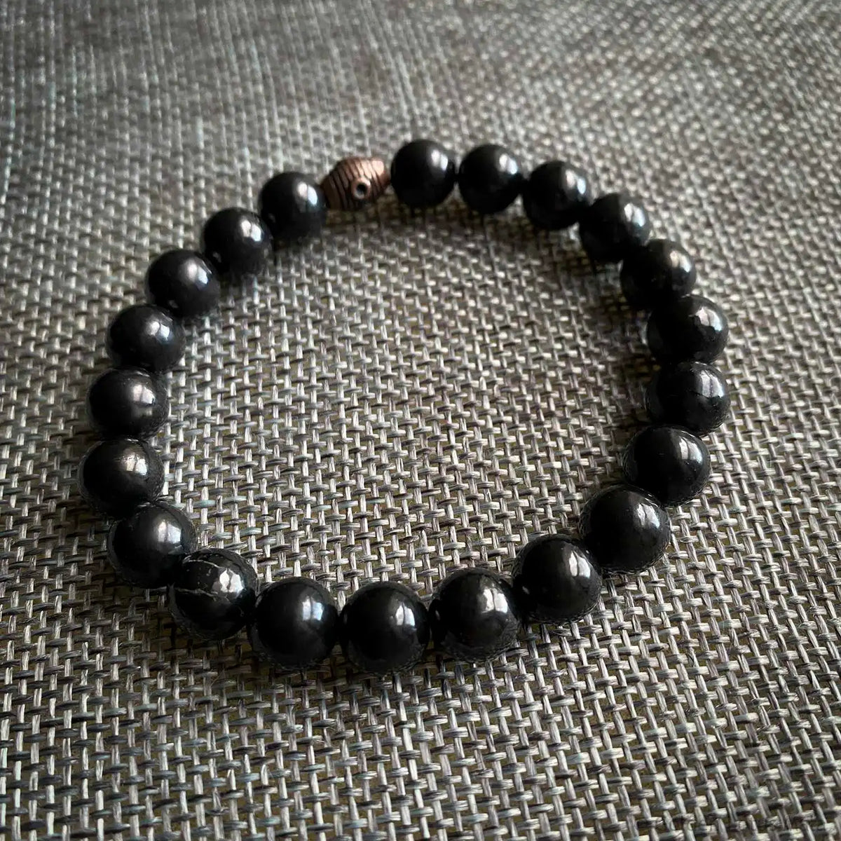 Black shungite beaded bracelet on a textured gray surface