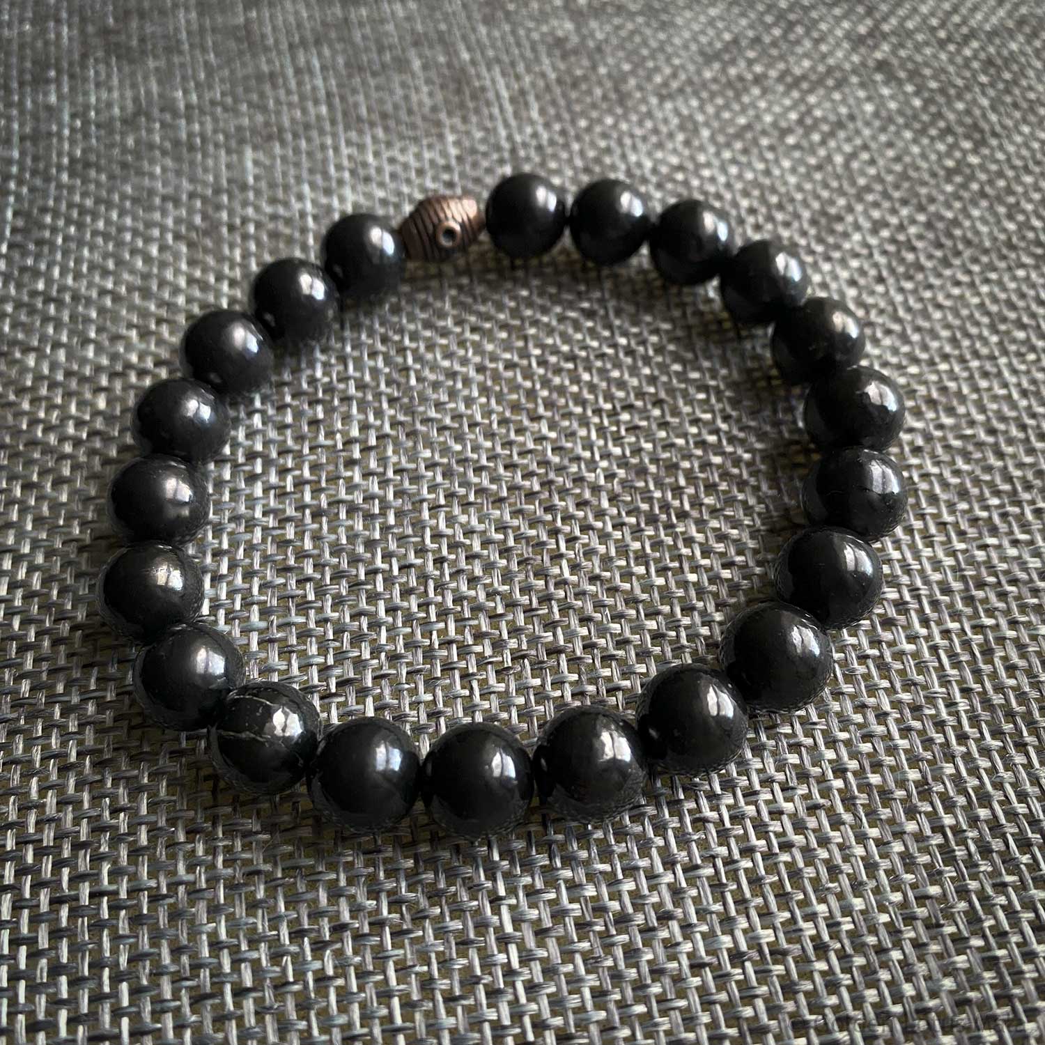 Black beaded Shungite bracelet on a textured gray surface