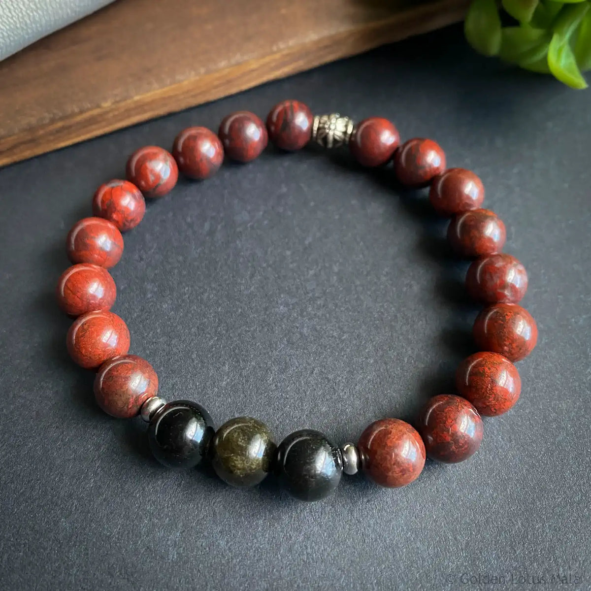 Natural stone bracelet with red and black round beads on a dark surface