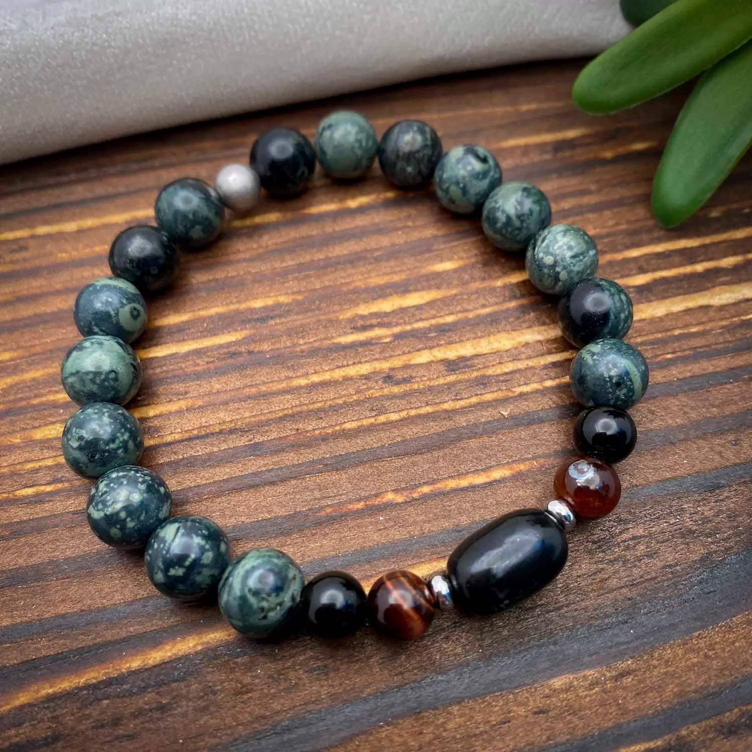 Beaded bracelet with green, black, and brown stones on a wooden surface