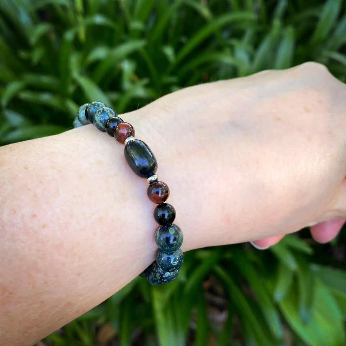 Shungite, jasper, tiger eye beaded bracelet on a wrist with a green leafy background