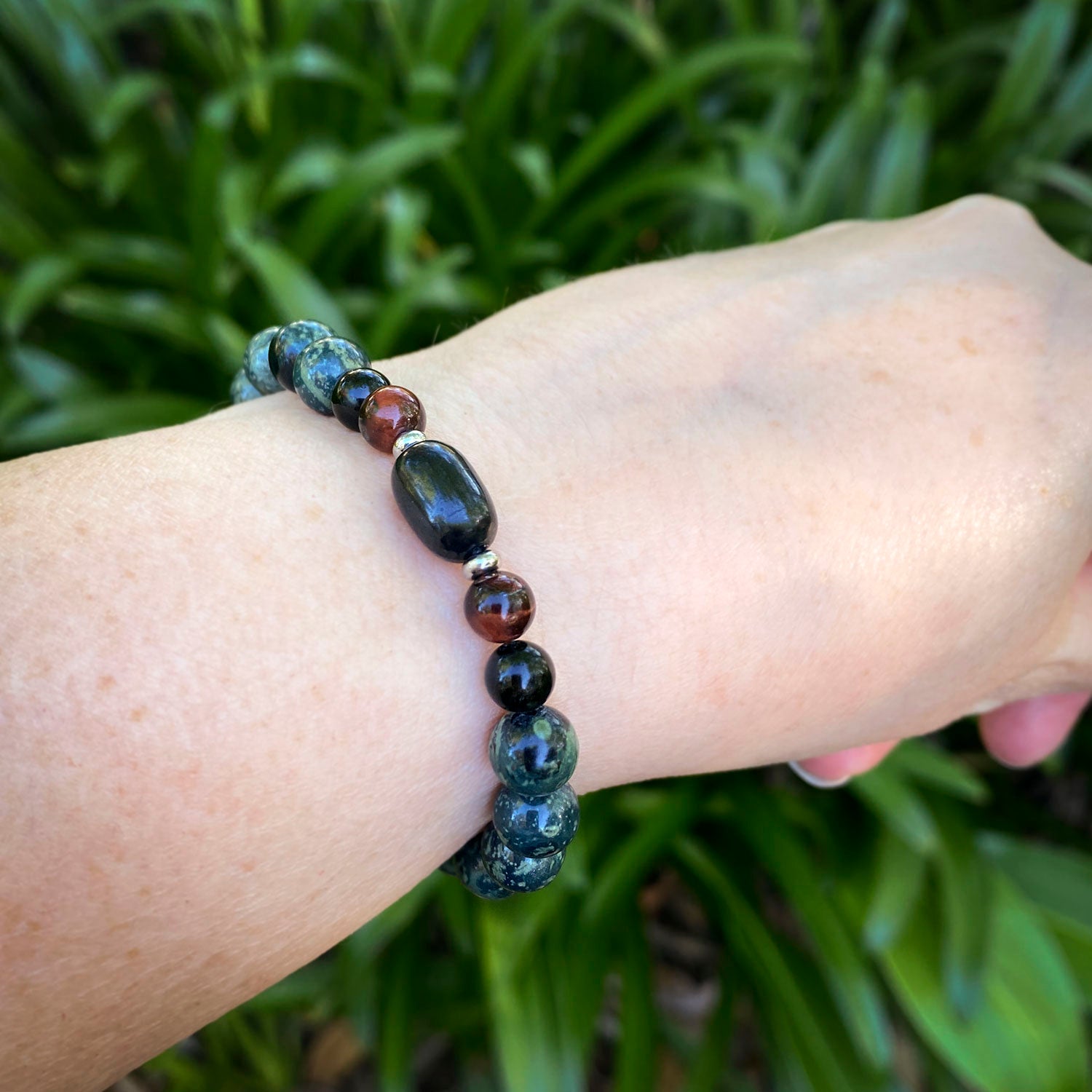 Bracelet with dark beads on a wrist against a green leafy background