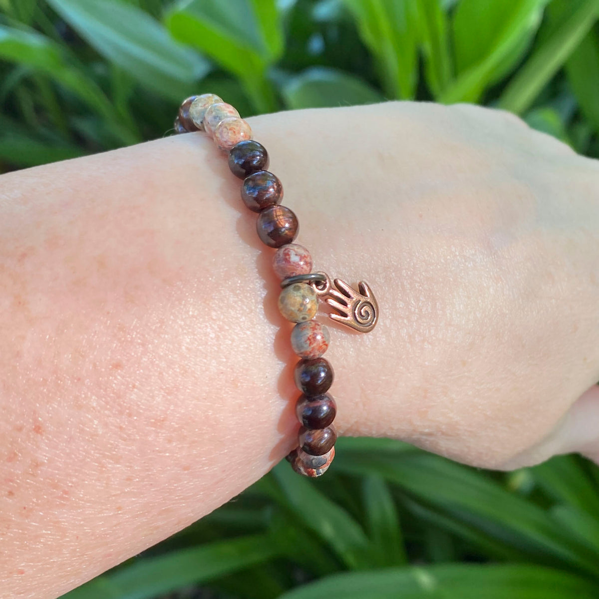 Beaded bracelet with a reiki charm on a wrist against a green leafy background