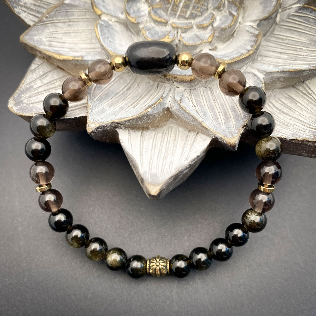 Black beaded bracelet with gold accents on a gray surface with decorative silver flower