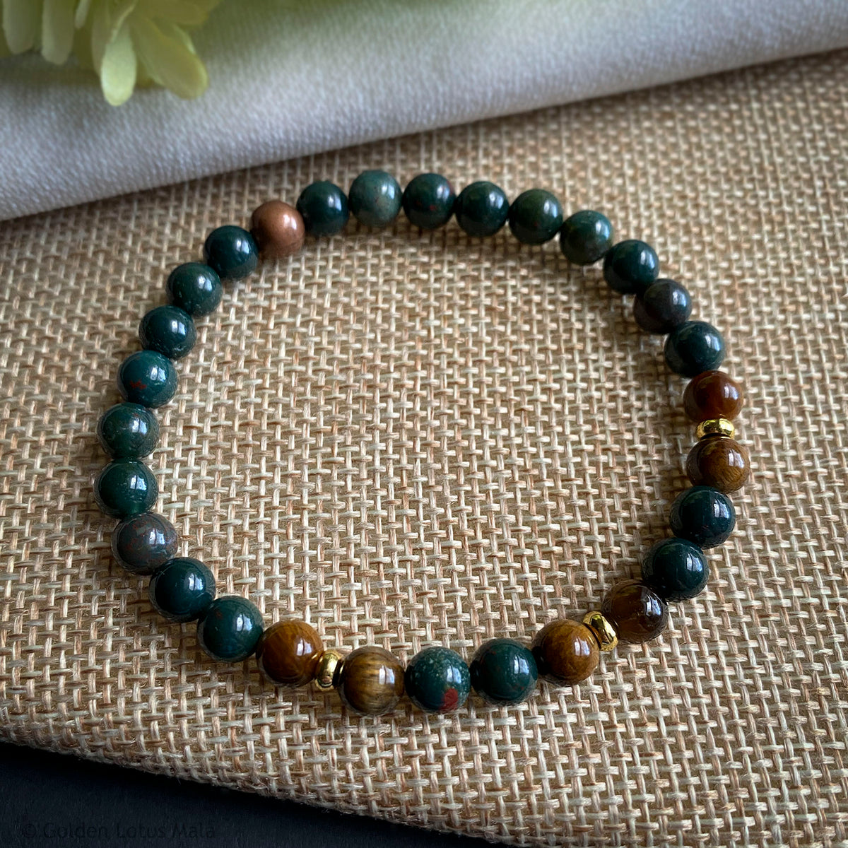Beaded bracelet with green and brown stones on a textured fabric background