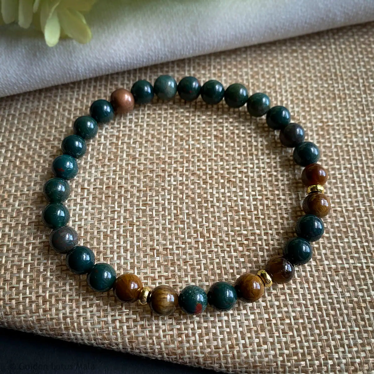 Gemstone beaded bracelet with green bloodstone and brown tigerseye round beads on a textured fabric background