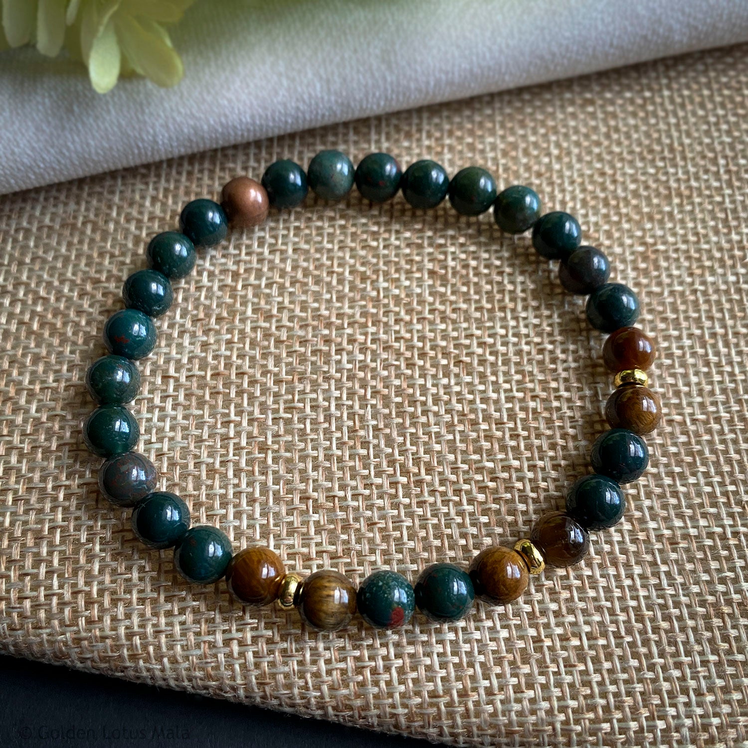 Beaded bracelet with green and brown stones on a textured fabric background