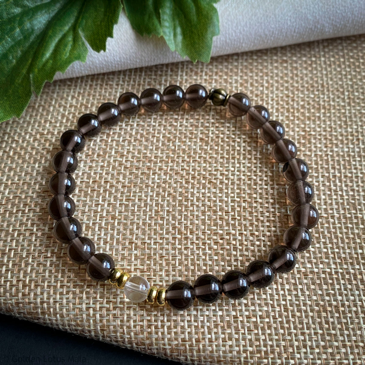 Beaded bracelet with dark beads and a clear crystal on a textured fabric background