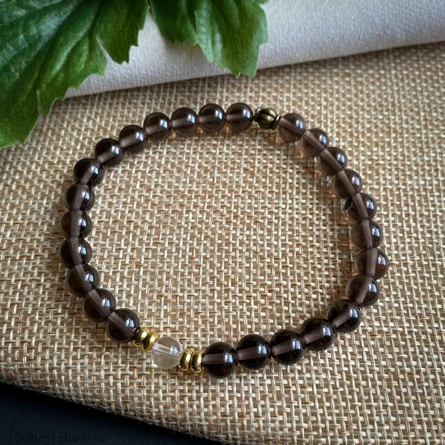 Beaded bracelet with smoky black and gold beads on a textured fabric background