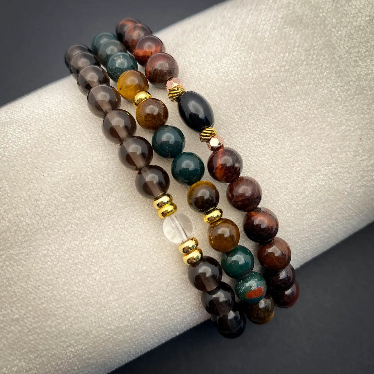 Three beaded bracelets with gold accents on a textured surface