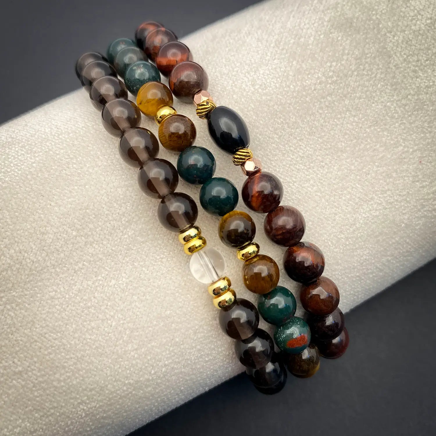 Three beaded bracelets with gold accents on a textured surface