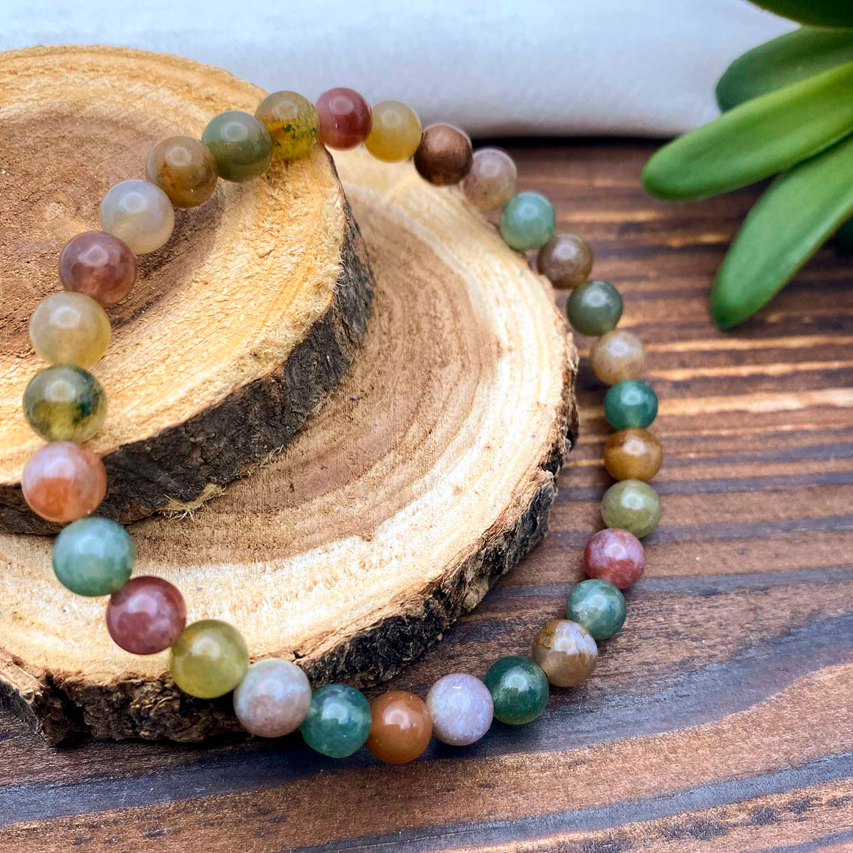 Multicolored agate beaded bracelet on a wooden surface with a plant in the background