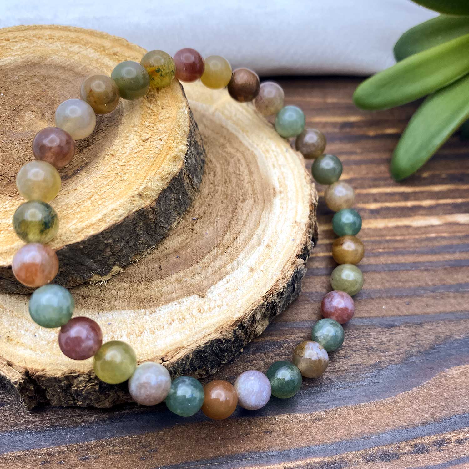 Multicolored agate beaded bracelet on a wooden surface with a plant in the background