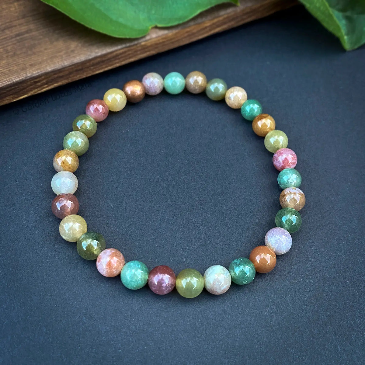 Multicolored beaded bracelet on a dark surface with green leaves in the background