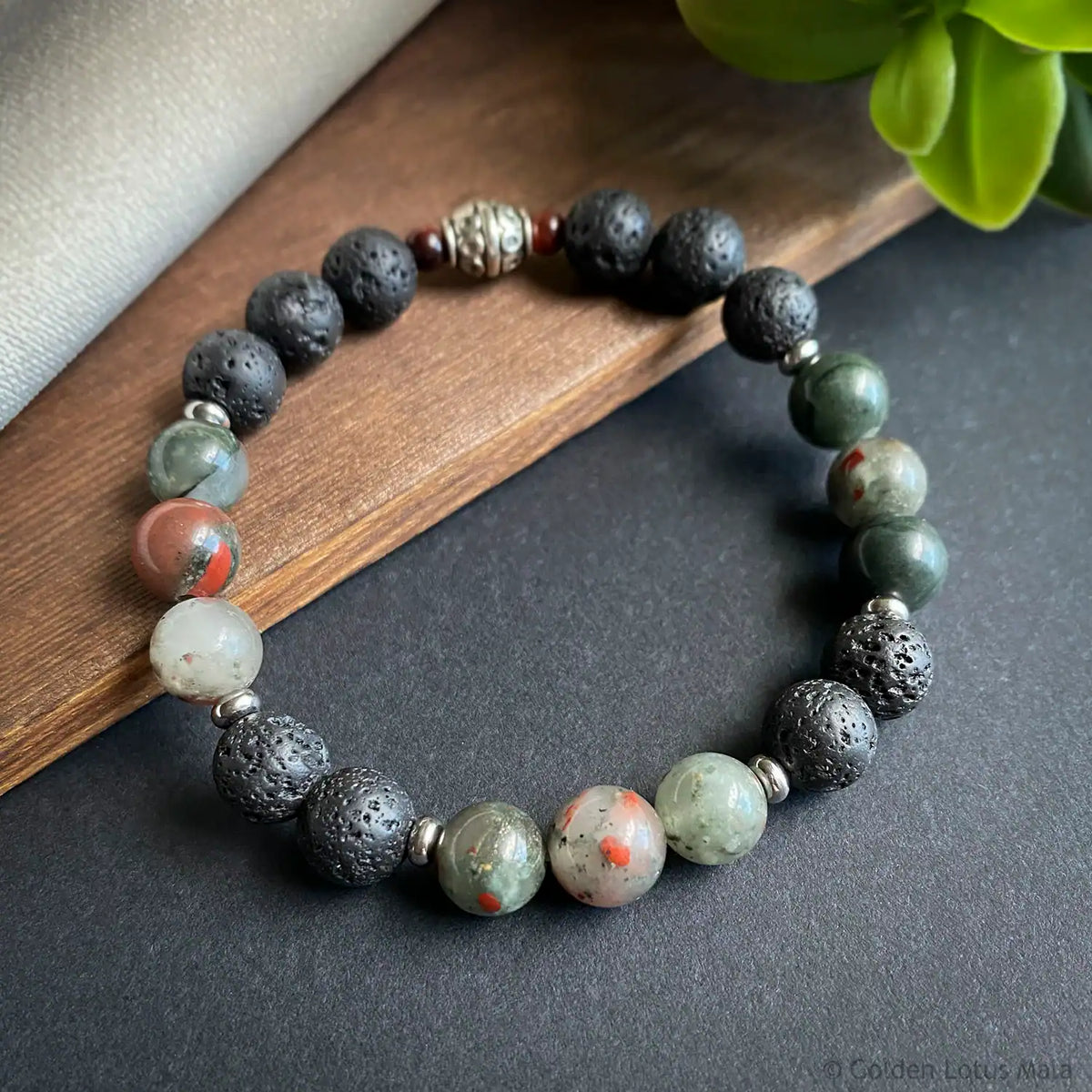 Multicolored gemstone beaded bracelet on a dark surface with a wooden block and plant in the background