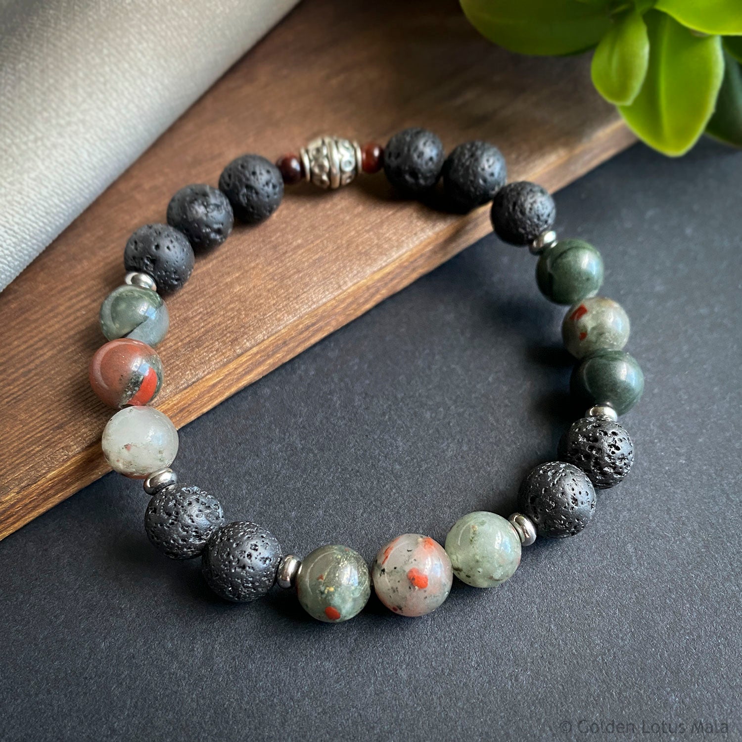 Multicolored beaded bracelet on a dark surface with a wooden block and plant leaf in the background.