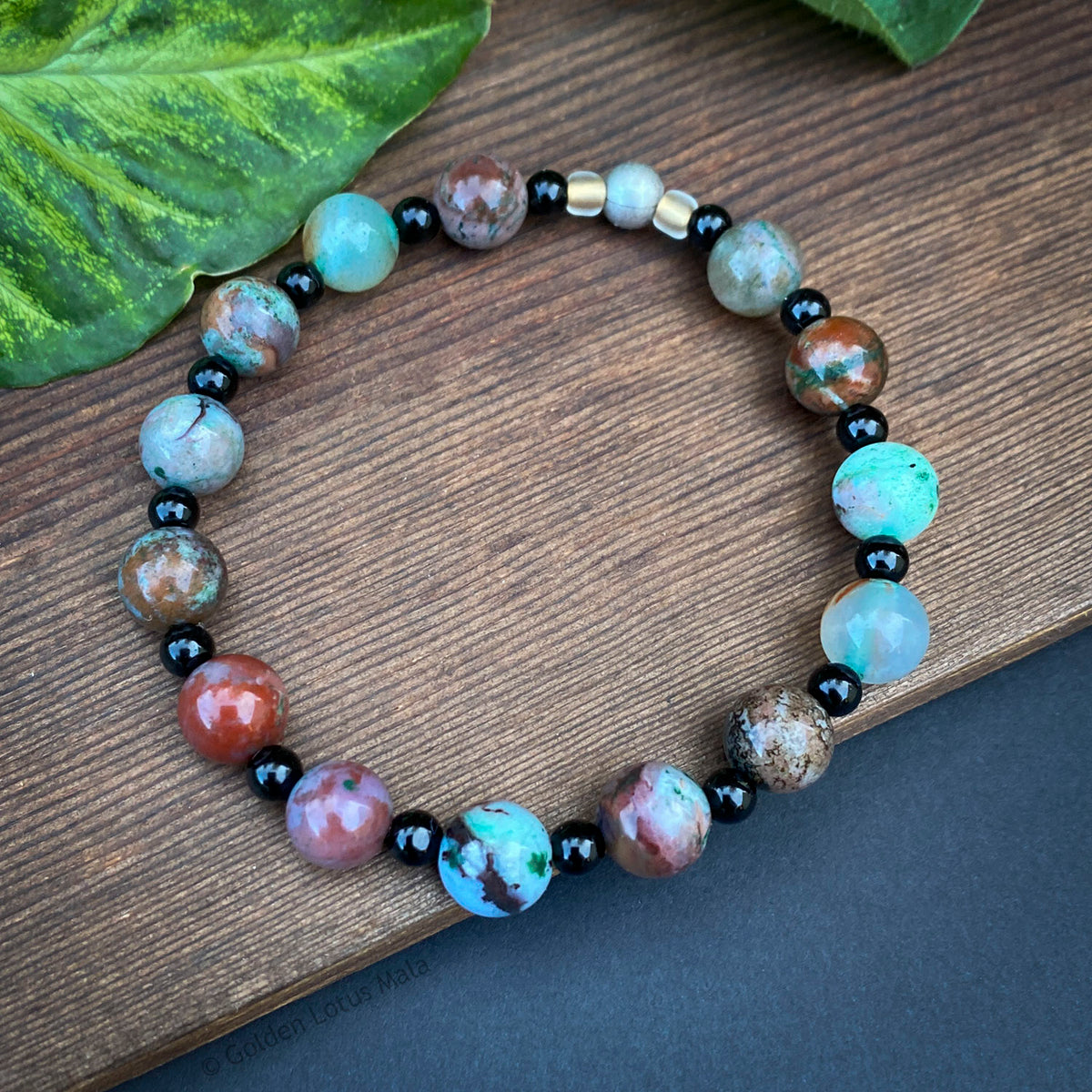 Multicolored Ecgolite beaded bracelet on a wooden surface with green leaves
