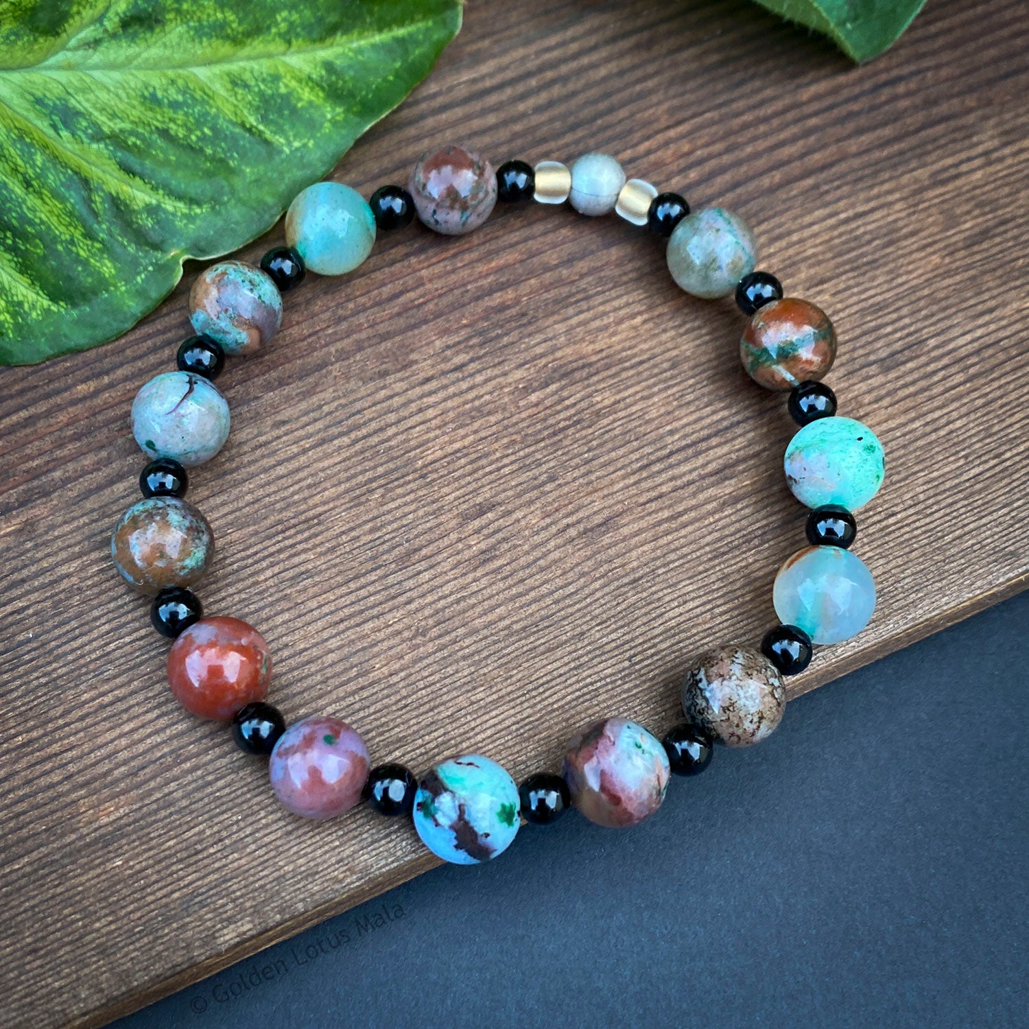 Multicolored Ecgolite beaded bracelet on a wooden surface with green leaves