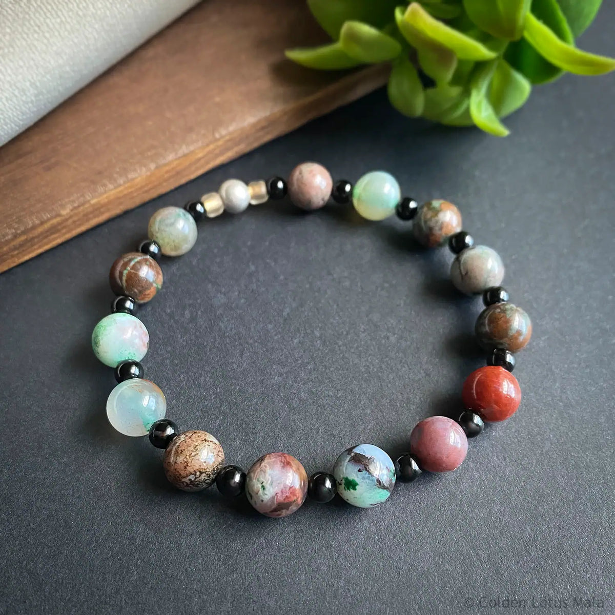 Multicolored beaded bracelet on a dark surface with a plant in the background