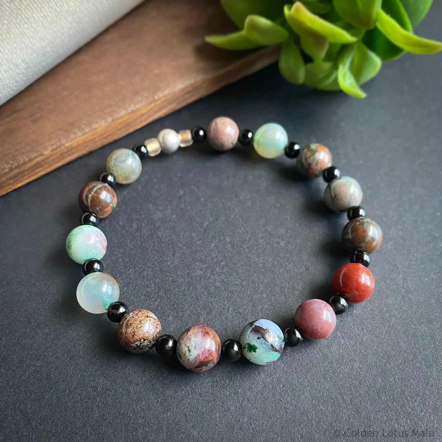 Multicolored beaded bracelet on a dark surface with a plant in the background