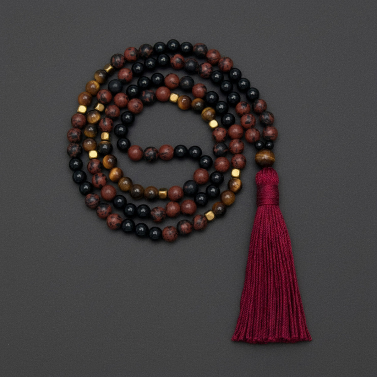 Mala necklace with multicolored obsidian and tigerseye beads with a red tassel on a dark gray background