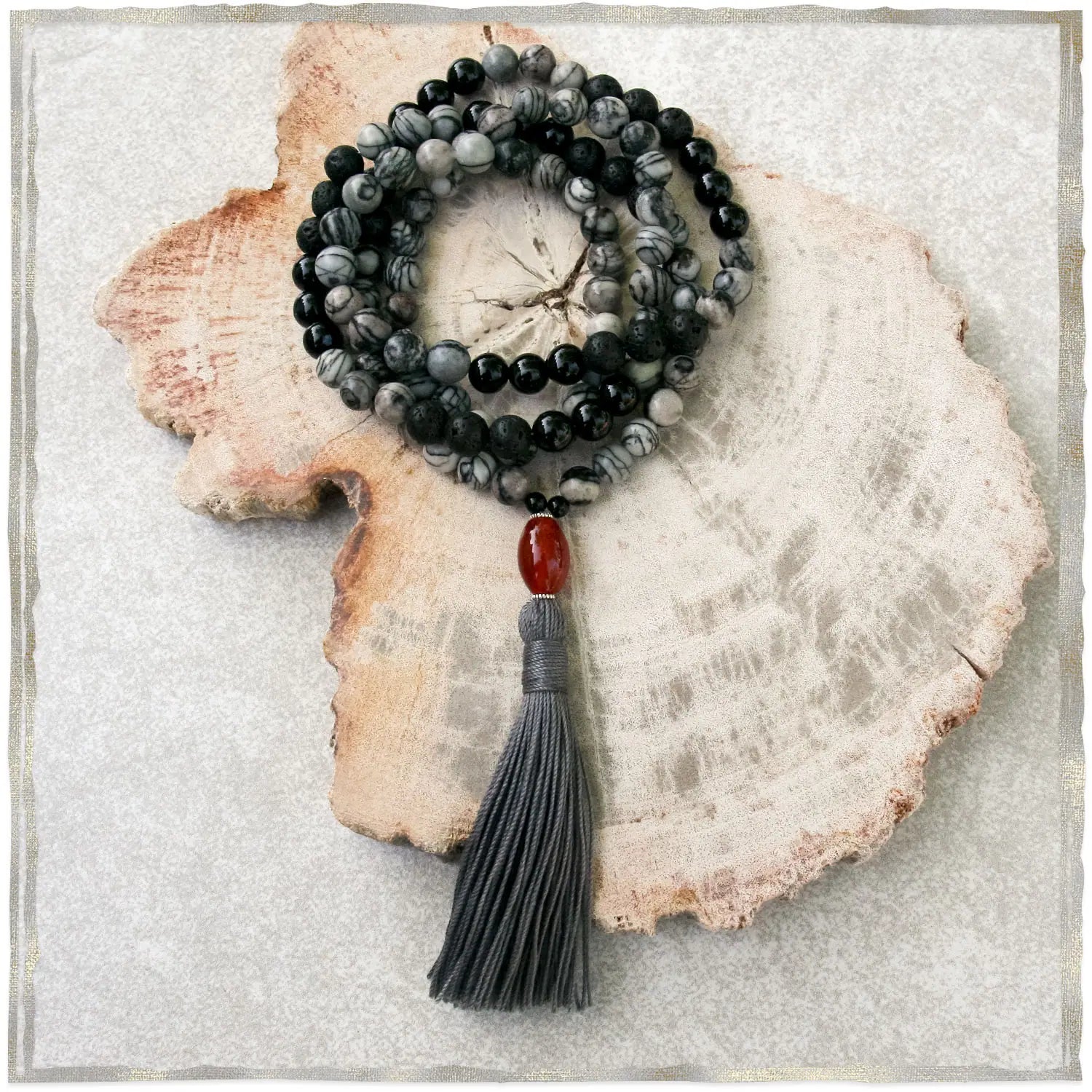 Gray and black beaded necklace with a tassel on a textured stone surface