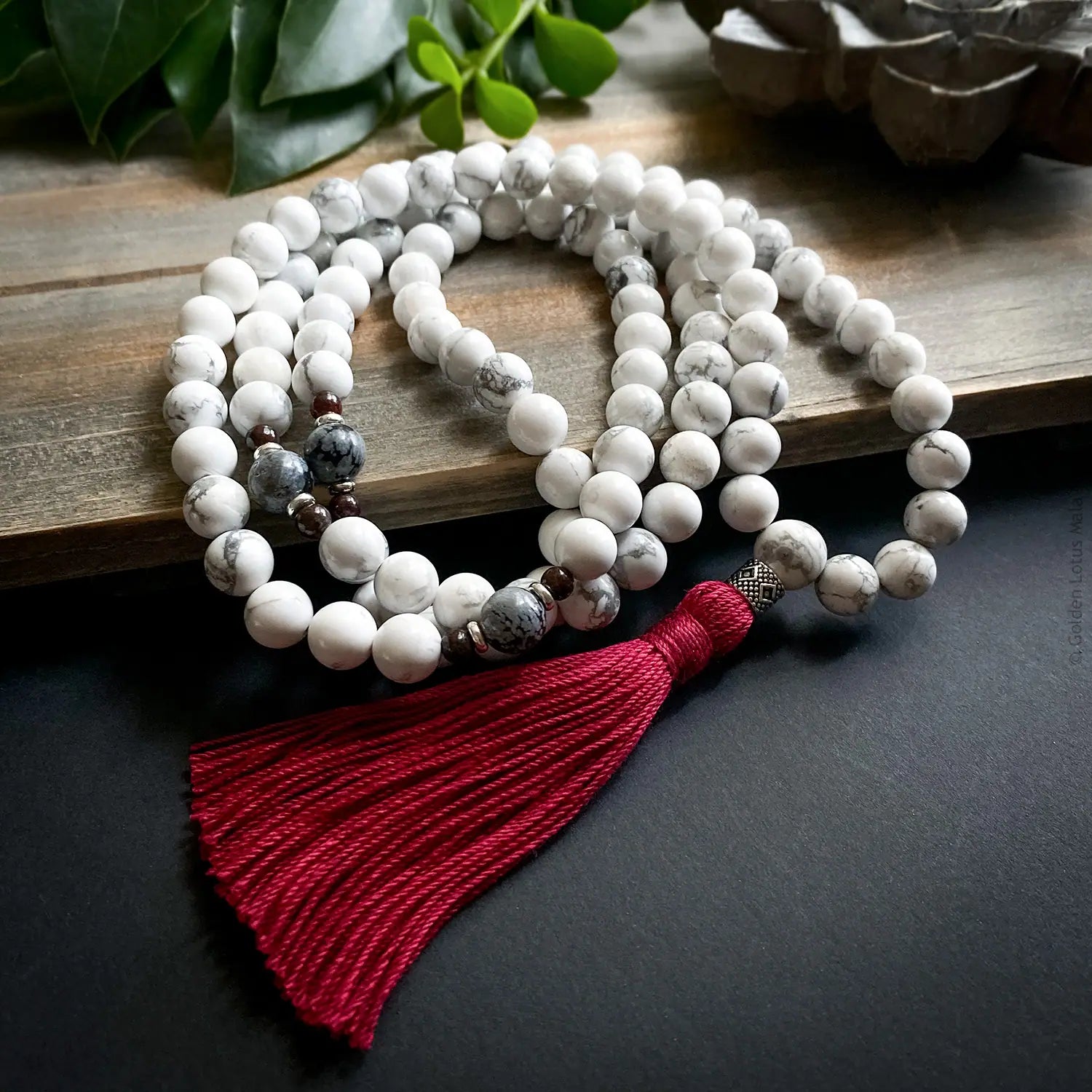White mala necklace with a red tassel on a wooden surface