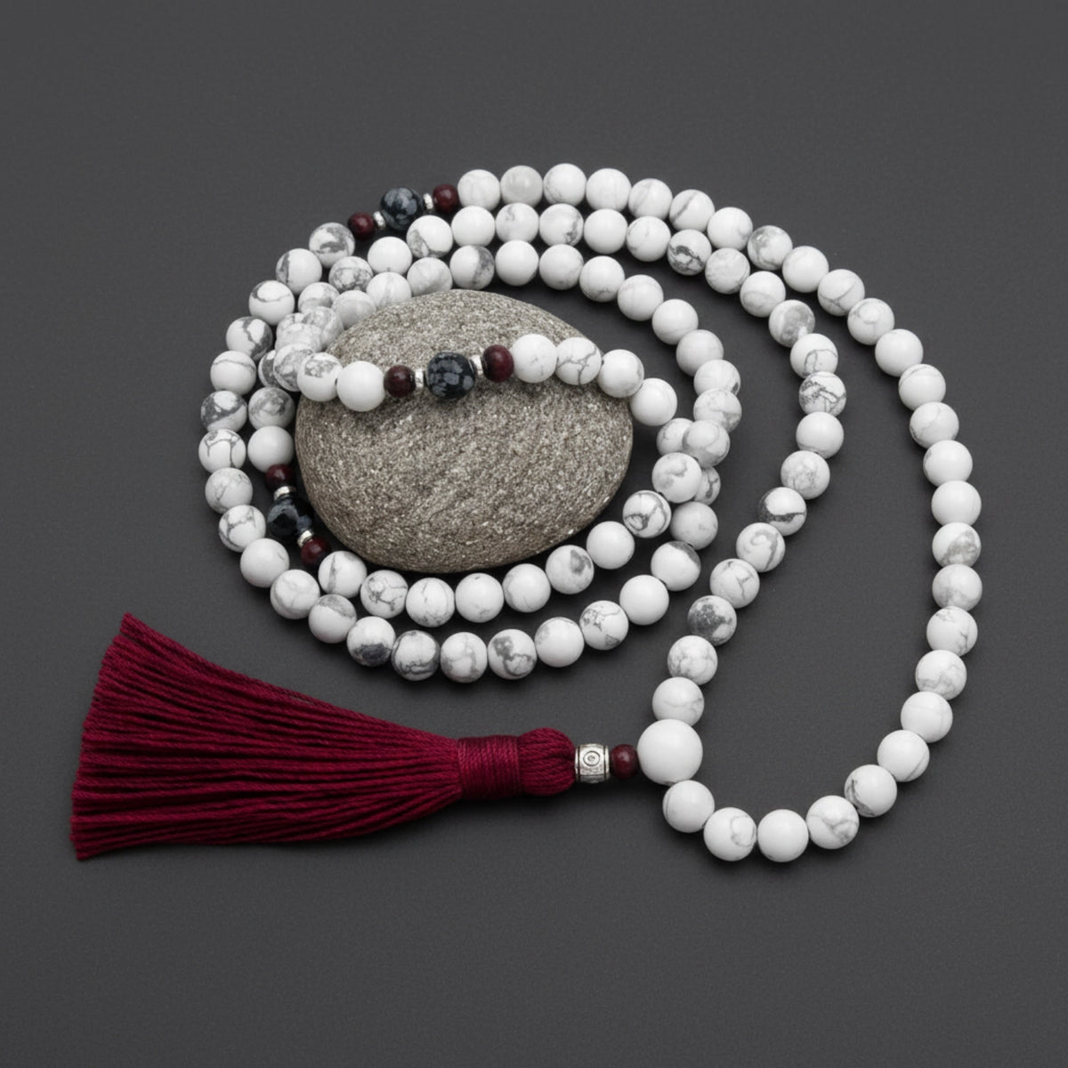 White mala beads with a red tassel on a dark gray background
