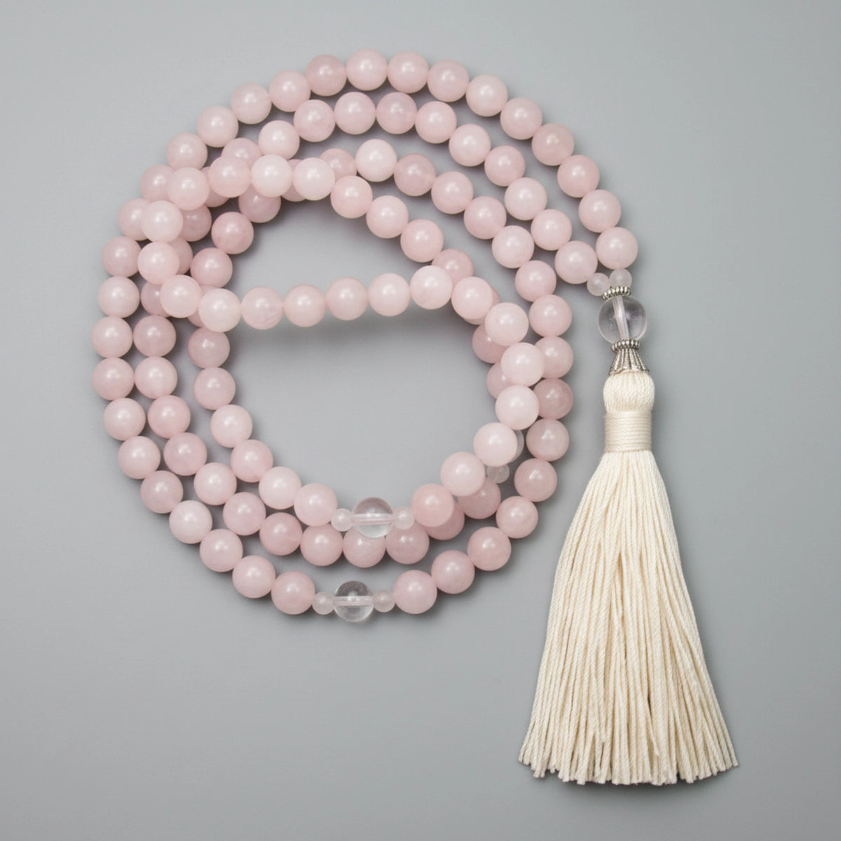 Pink rose quartz beaded mala with a white tassel on a gray background