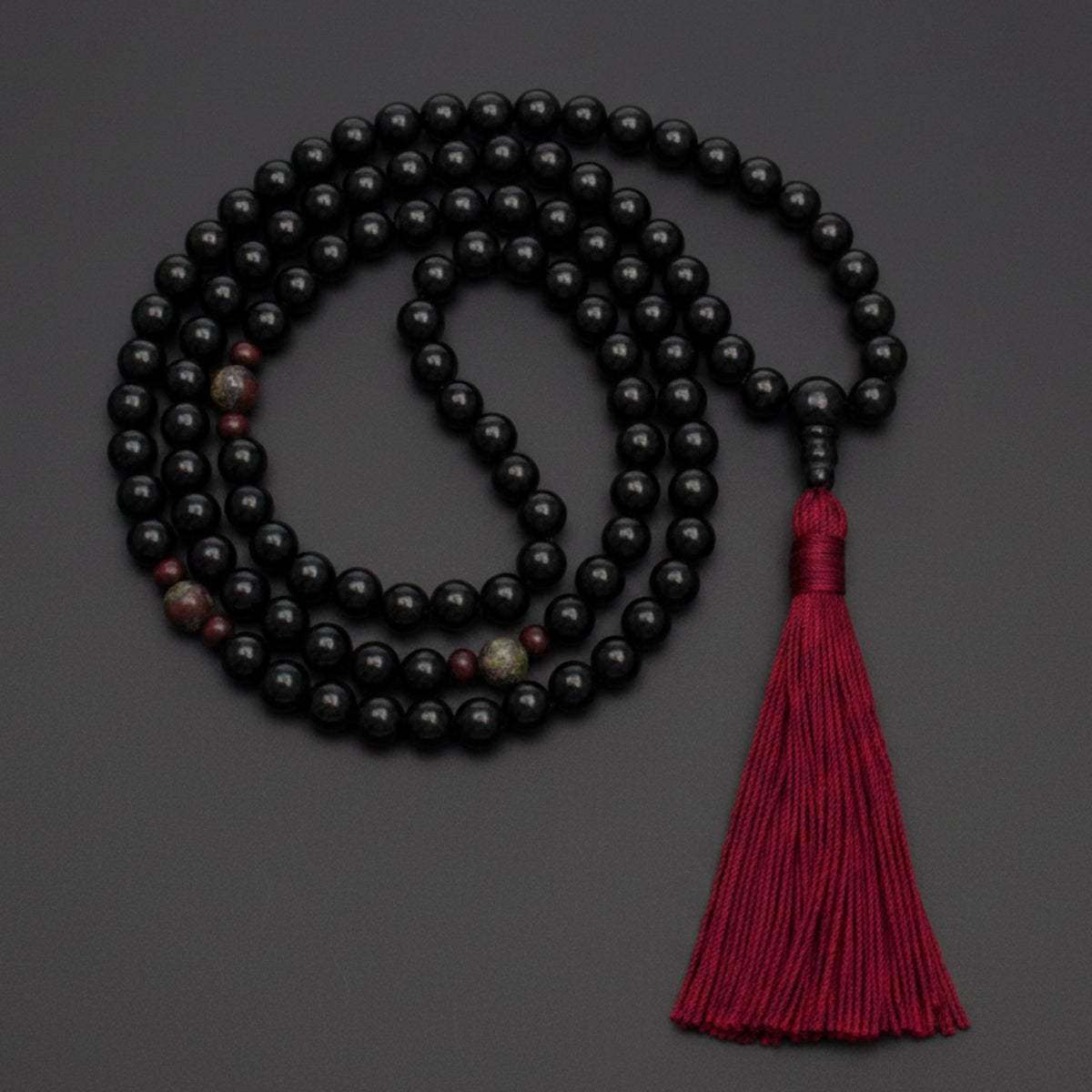 Black onyx mala necklace with a red tassel on a dark background