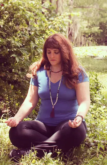 A women wears a mala necklace in nature during meditation.