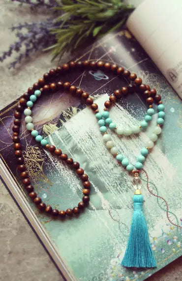 A mala made of wood and gemstone beads lying on a book.